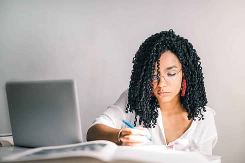 woman in white polo shirt holding a pen near laptop